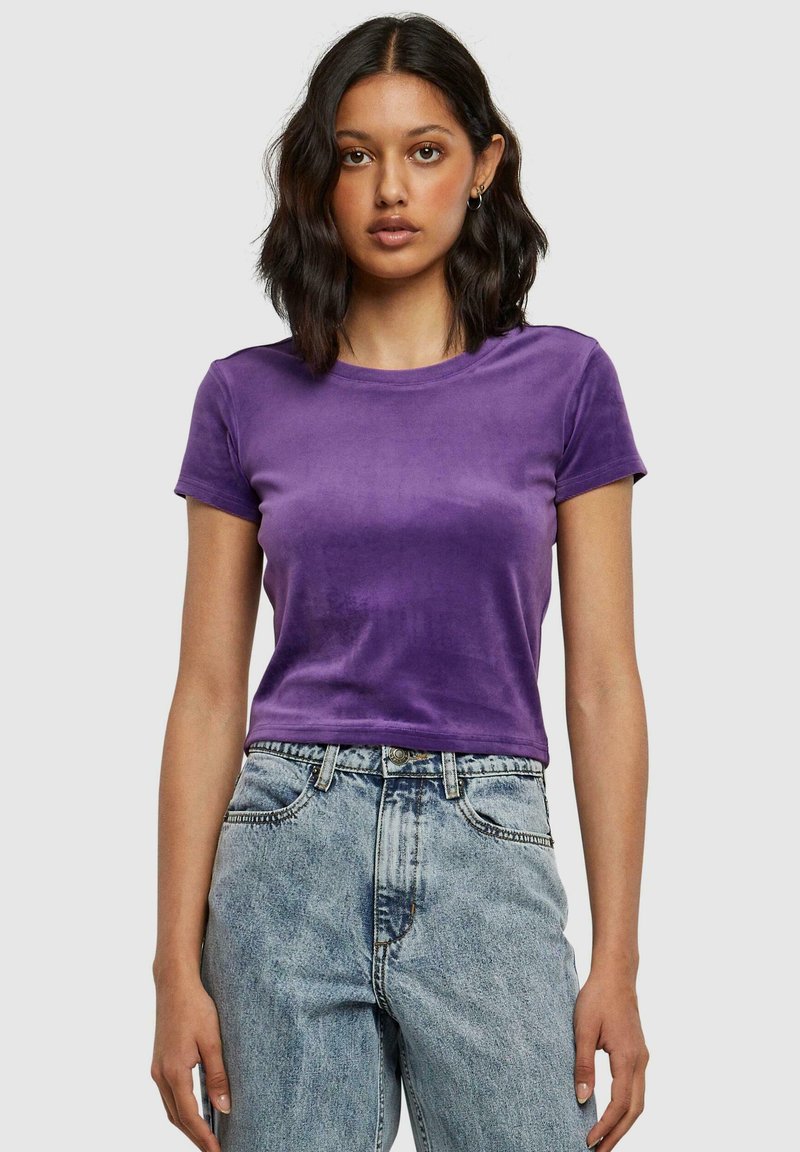 Paarse fluwelen t-shirt met korte mouwen, ronde hals, getailleerd ontwerp, gecombineerd met high-waisted lichte denim jeans. Zachte textuur.