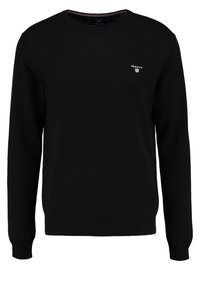Schwarzer Strickpullover mit rundem Halsausschnitt. Verfügt über gerippte Bündchen und Saum, ein kleines gesticktes Logo auf der Brust und eine glatte Textur.