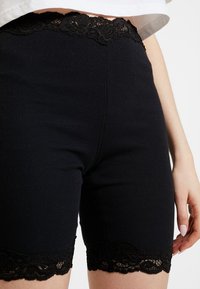 Svarta ribbade shorts med spetsdetaljer vid fållen. Tajt passform med en slät yta och strukturerad midjeband.