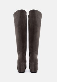 Καφέ σουέτ μπότες μέχρι το γόνατο με λεία υφή, τετράγωνες τακούνια και ορατά φερμουάρ στο πίσω μέρος, με εφαρμοστή γραμμή και καθαρές γραμμές.