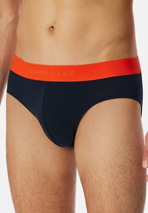 Navyblå kalsonger gjorda av slät tyg, med ett klart orange elastiskt midjeband där varumärket "Schiesser" är präglat.