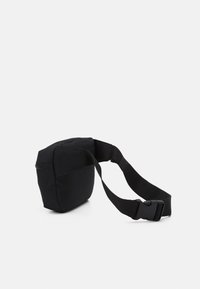 Musta kangasristilaukkku suorakaiteen muotoinen, säädettävä hihna ja toisella puolella vetoketjullinen tasku. Sileä pinta, minimalistinen muotoilu.