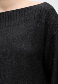 Gros plan d'un pull en maille gris foncé avec un large col côtelé reposant sur une épaule.