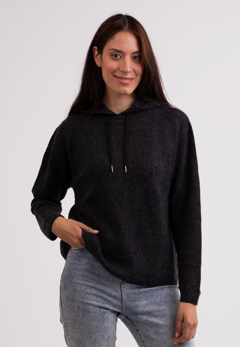 Felpa in pile grigia scura con una vestibilità comoda, coulisse e maniche lunghe. Indossata con jeans in denim azzurro chiaro, con dettagli sulle tasche.