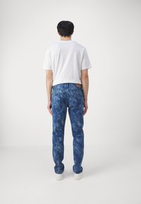Blå marmorert mønster denim med rett snitt, som har fem lommer og en brun etikett på baklivet, sammen med en hvit t-skjorte.