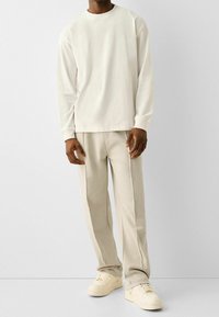 Off-white långärmad skjorta i kombination med ljusbeiga byxor och krämfärgade sneakers. Outfiten har en avslappnad passform och enkelt design.