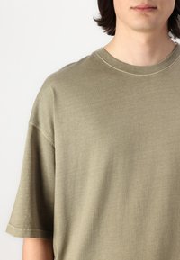Olivengrøn T-shirt med korte ærmer lavet af blødt bomuld; afslappet pasform med rund halsudskæring og minimale syninger.