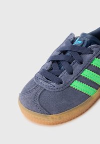 Σκούρο μπλε σουέντ αθλητικό παπούτσι με πράσινες ρίγες, με υφή από καουτσούκ στη σόλα, κορδόνια και επενδυμένο γιακά στον αστράγαλο.