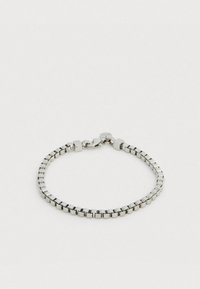 Brățară din metal argintiu cu zale pătrate cu finisaj neted, prinsă cu o închizătoare tip homar și o etichetă mică circulară cu marca.