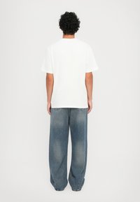 White cotton t-shirt with short sleeves, relaxed fit. Paired with light-wash, loose-fitting denim jeans featuring subtle fading.