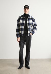 Checkered, fleece jacket in blue, white, and gray; black turtleneck; black jeans; black leather boots; cap with "BOSS" logo.