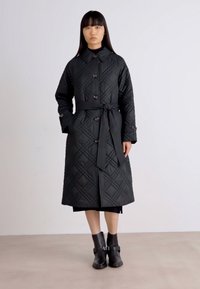 Μαύρο καπιτονέ παλτό με γιακά, μπροστινά κουμπιά και ζωνάκι στη μέση. Διαθέτει διαμαντέ σχέδιο και μακριά μανίκια για επιπλέον ζεστασιά.