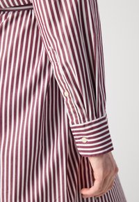 Camicia a maniche lunghe a righe bordeaux e bianche; tessuto in cotone; presenta un polsino con bottoni e cuciture bianche a contrasto.