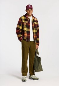 Punaisen, keltaisen ja mustanruudullinen fliisinen flanellitakki, valkoinen t-paita, oliivinvihreät samettihousut, harmaat tennarit ja oliivinvihreä kangaskassi.