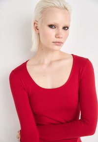 Rotes Langarmshirt mit Rundhalsausschnitt, aus dehnbarem Stoff, mit figurbetontem Schnitt und glatter Textur.