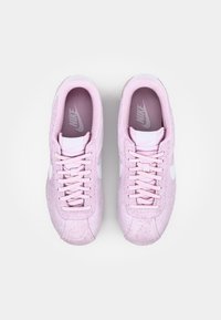 Nike sneakers featuring a soft pink suede upper, white accents, and laces. Thick rubber sole with textured grip and cushioned interior.