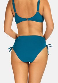 Zestaw bikini w kolorze teal, z topem na plecach w kształcie łódki, regulowanymi ramiączkami oraz wysokim dołem z marszczeniami po bokach i wiązaniami. Gładka tekstura.