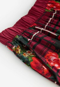 Red floral patterned shorts with a black plaid design, featuring an elastic waistband and smooth fabric texture.