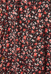 Svart tyg med små röda och vita blommönster och synliga bruna knappar längs ena sidan.