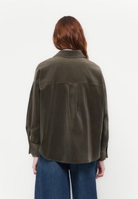 Olivgrünes Kordhemden mit Rückenpasse, subtiler Textur und langen Ärmeln. Mit abgerundetem Saum und geknöpften Manschetten.