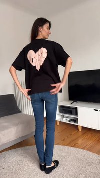 Camiseta negra de gran tamaño con un gran diseño de corazón rosa texturizado en la parte trasera. Combinada con vaqueros ajustados azules y zapatos negros.