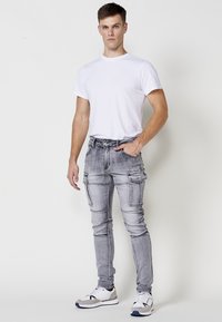 Grijze cargobroek met meerdere zakken, een slim fit en een lichte vervaging, gecombineerd met een effen wit T-shirt en witte sport sneakers.