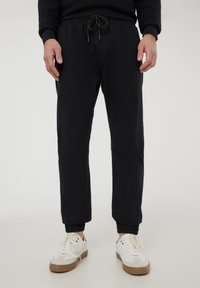 Pantaloni jogger neri realizzati in tessuto morbido, dotati di vita elasticizzata con cordoncino, polsi a costine e dettagli di cucitura sulle ginocchia.