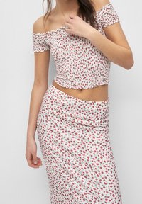 Floral two-piece set featuring a smocked off-the-shoulder top with ruffled edges and a matching skirt, both in white with red and green patterns.
