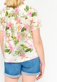 Short-sleeve shirt made of lightweight fabric, featuring a floral pattern with pink flowers and green leaves, paired with denim shorts.