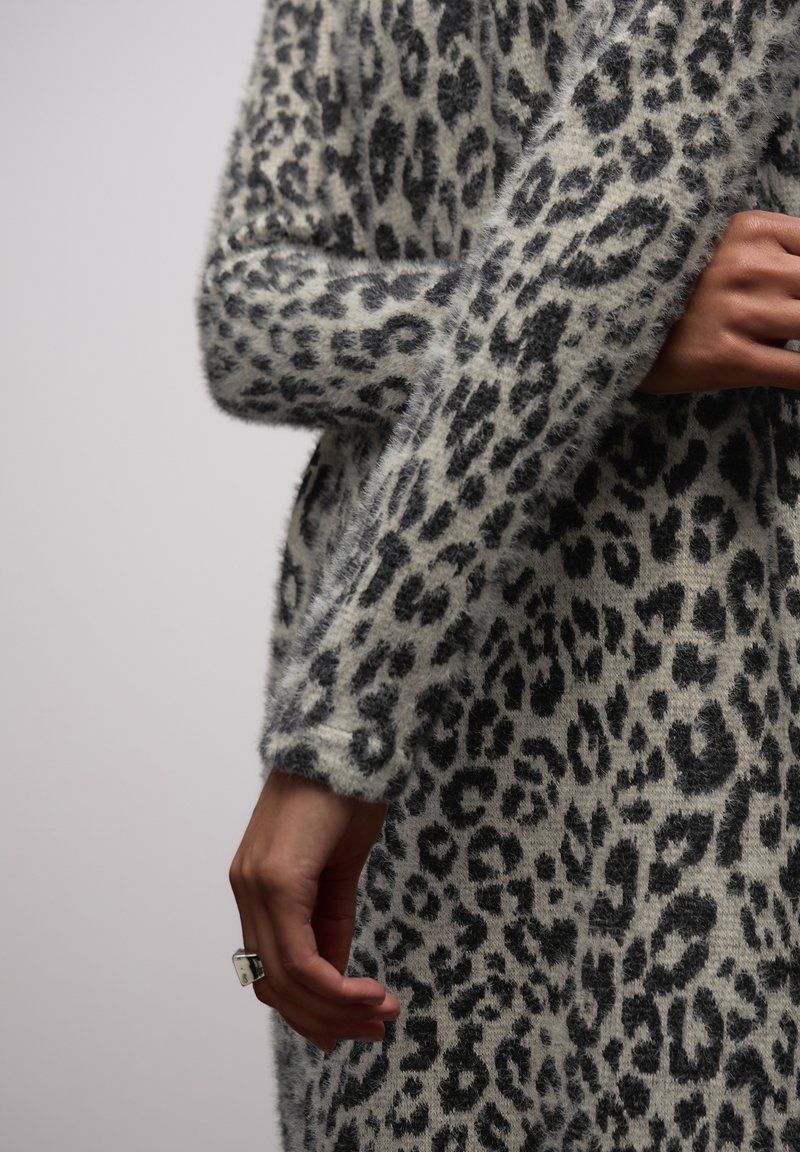 Maglione leopardato beige e nero con una texture pelosa, caratterizzato da maniche lunghe e una vestibilità rilassata, messo in risalto da un elegante anello alla mano.