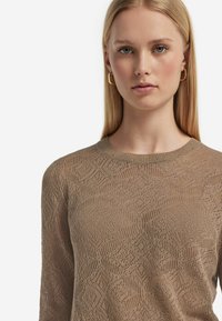 Maglione lavorato a maglia marrone chiaro con un motivo testurizzato, scollatura rotonda e maniche lunghe, dal taglio ampio e con un tessuto leggero e traspirante.