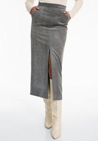 Grauer Cord-Midi-Rock mit seitlichem Schlitz, verfügt über Fronttaschen und einen taillierten Bund. Kombiniert mit knielangen cremefarbenen Stiefeln.