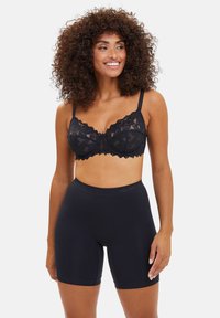 Sostén de encaje negro con bordes de forma ondulada y costuras decorativas, combinado con pantalones cortos negros ajustados, hechos de una tela suave y elástica.