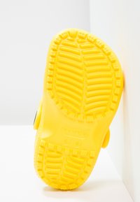 Semelle de chaussure en caoutchouc jaune avec un profil texturé, dotée de rainures profondes et de motifs en relief pour une meilleure adhérence. Étiqueté clairement "crocs" sur la surface.