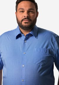 Ljusblå kortärmad skjorta gjord av mjukt tyg, med knappad krage, bröstficka och subtil struktur.