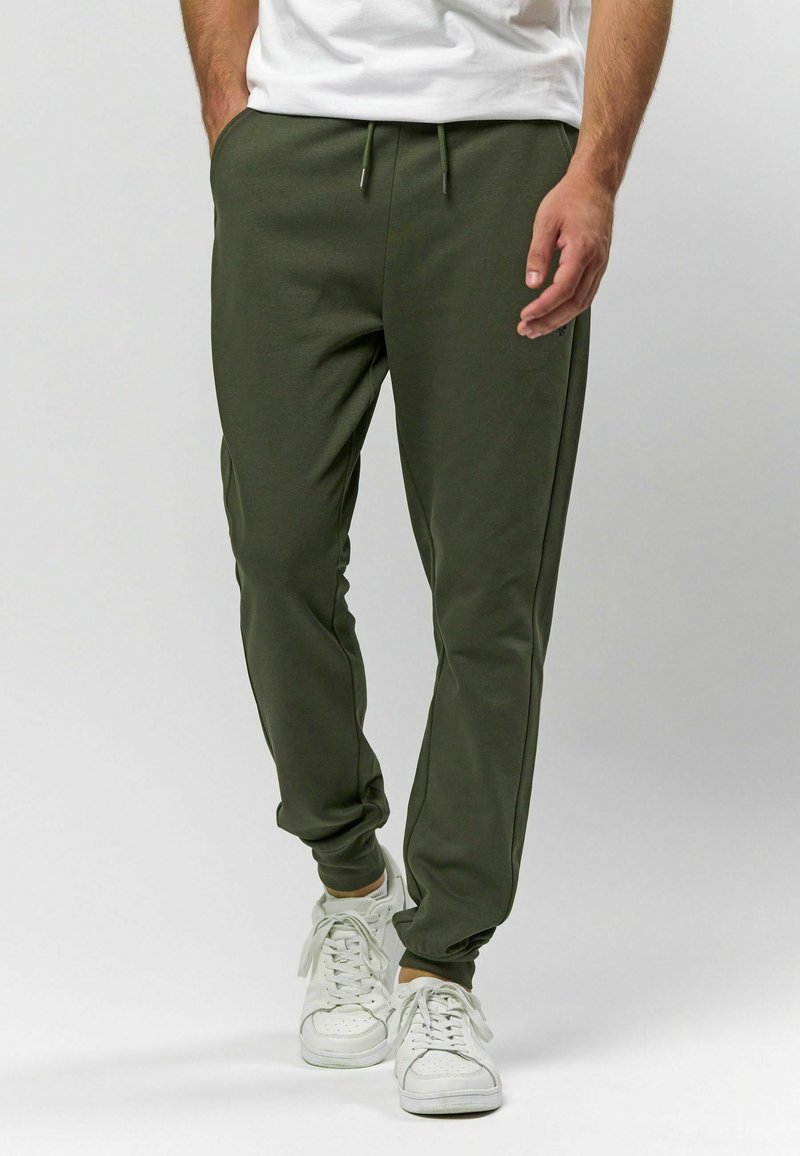 Olivové nohavice vyrobené z mäkkého materiálu, s elastickým pásom a šnúrkou, bočnými vreckami a prispôsobenými manžetami na členkoch.