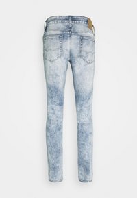 Pantalones vaqueros de mezclilla azul claro con textura desgastada, cinco bolsillos y una etiqueta de cuero marrón en la cintura. Diseño de pierna cónica.