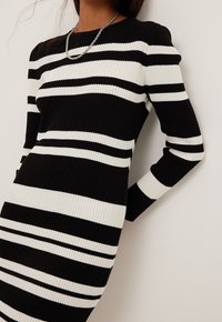 Abito a righe bianche e nere con maniche lunghe, caratterizzato da righe di larghezza variabile e un design a collo rotondo.