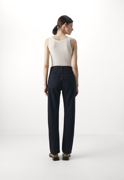 Hvit ribbet tanktop kombinert med høyt midje mørk denim jeans. Jeansene har en rett ben design og to baklommer.