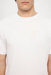 Hvid bomulds t-shirt med et diskret prægning af logoet "EA7 EMPORIO ARMANI" på brystet, med en klassisk rund hals og korte ærmer.
