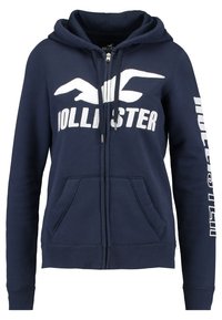 Marin zip-up hoodie tillverkad av bomullsblandning, med vit "Hollister"-logotyp och kängurufickor; inkluderar huva med dragsko.