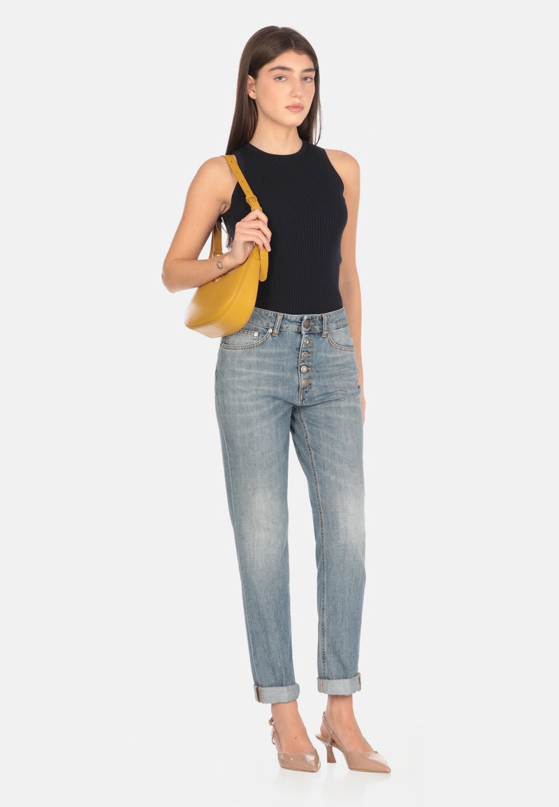 Top senza maniche a coste in blu navy, pantaloni in jeans a vita alta di un blu chiaro con chiusura a bottoni, e tacchi a punta beige. Una borsa a spalla gialla completa l'outfit.