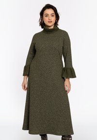 Robe en tricot longue, vert olive, avec un col montant, des manches évasées et une finition texturée. Le design est simple, sans motifs ni ornements.