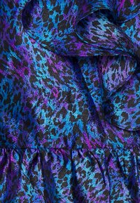 Jasny materiał na czarnym tle zdobi niebieski i fioletowy wzór w panterkę, ukazujący fakturę i falbany.