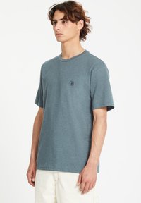 T-shirt gris-bleu à col ras du cou, manches courtes, texture douce, détail de logo subtil sur la poitrine, coupe décontractée, en coton.