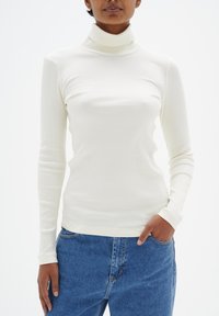 Geripptes Turtleneck-Oberteil in Off-White, mit langen Ärmeln und schmaler Passform, kombiniert mit lockeren blauen Denim-Jeans. Glatte Textur.