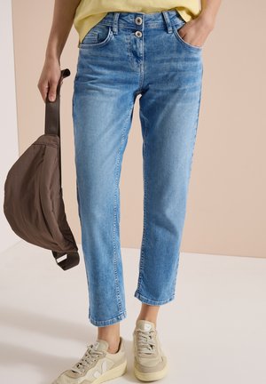 Person iført lyseblå jeans med høj talje og beige sneakers, der holder en brun crossbodytaske i stroppen.