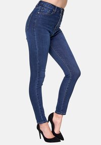 Jeans ajustados de cintura alta en denim azul oscuro con costuras elegantes. Combinados con tacones negros de punta afilada, que muestran un ajuste ceñido y un suave brillo.