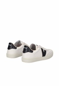 Sneakers in pelle bianca con accenti neri, caratterizzate da una punta rotonda, design con lacci e logo a contrasto sul tallone. Suola piatta.