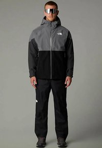 Waterdicht jas- en broekset in grijs en zwart, met een ritssluiting, verstelbare capuchon en meerdere zakken. Voorzien van reflecterende accenten.